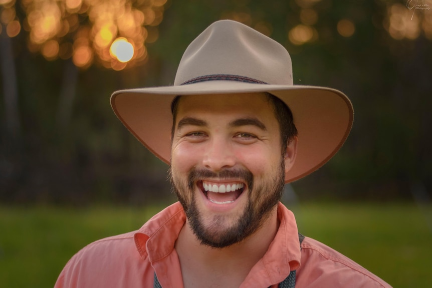 Close up of a dark haired man wearing an Akubra hat and smiling at the camera