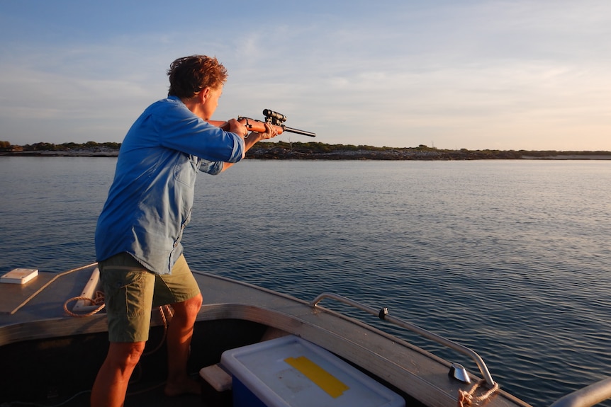 A woman holding a rifle and standing at the front of a boat on the ocean.