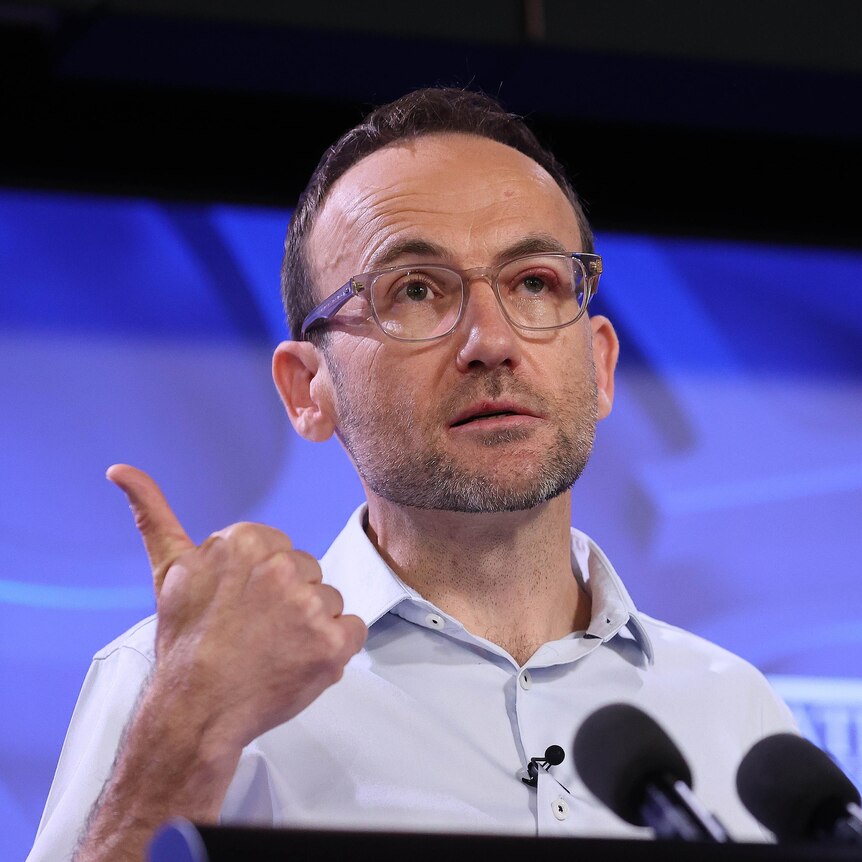 Adam Bandt stands behind a lectern with his thumb up.