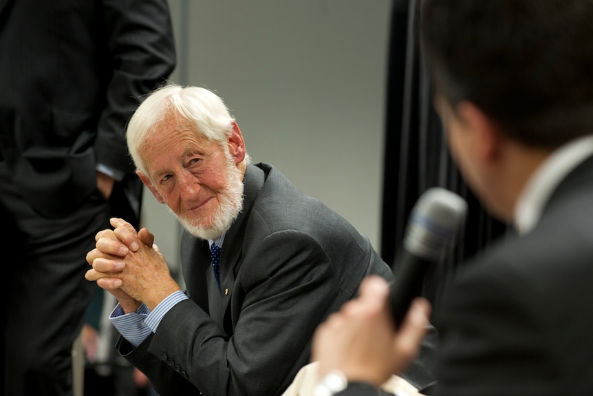 An elderly gentleman leans forward to answer a man holding a microphone