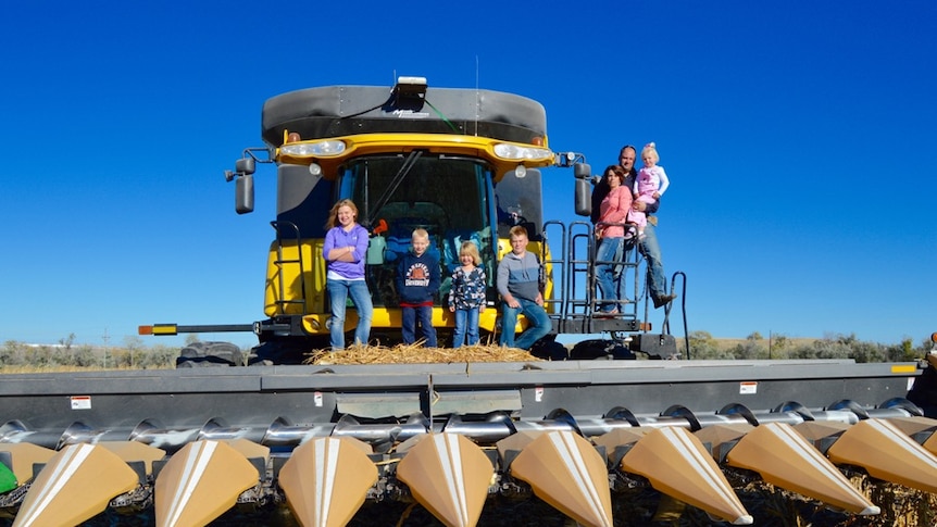 A family standing on a corn harvester in a paddock in the united states