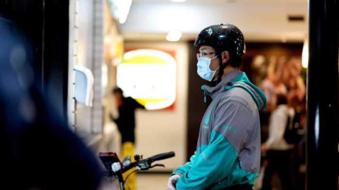 A masked food delivery driver waiting on an order at a fast food restaurant 
