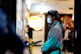 A masked food delivery driver waiting on an order at a fast food restaurant 