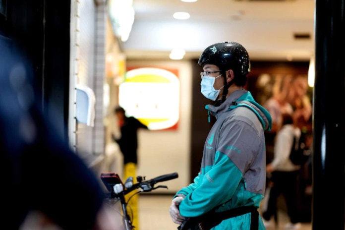 A masked food delivery driver waiting on an order at a fast food restaurant 