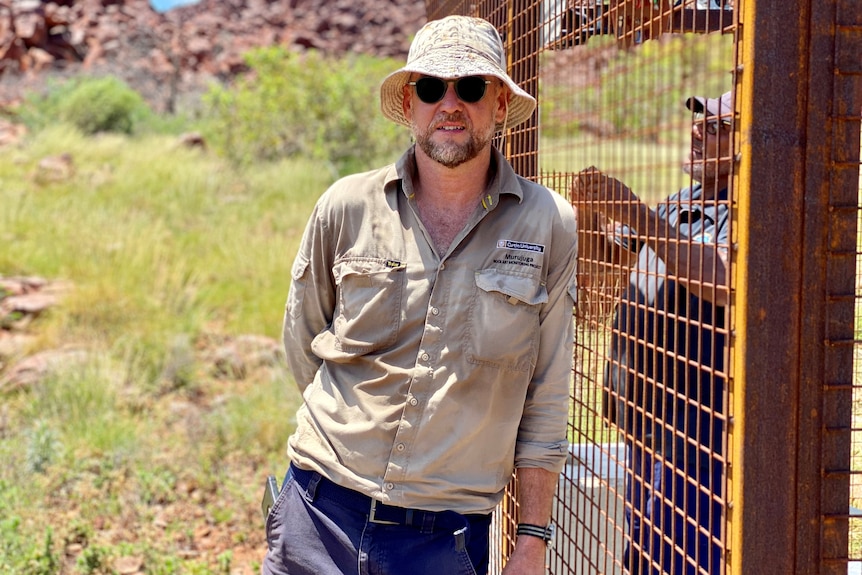 A man wearing a bucket hat, leaning against a metal cage