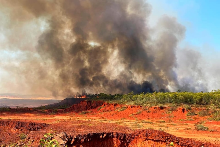 Smoke from a bushfire burning on the Dampier Peninsula, north of Broome, with red soil in the foreground