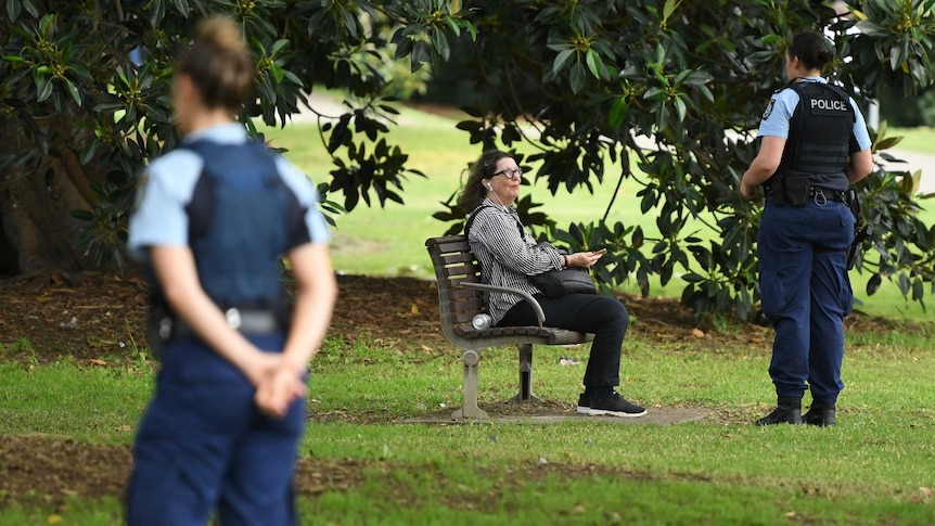 A police officer speaks to a woman sitting on an outdoor bench during the coronavirus outbreak