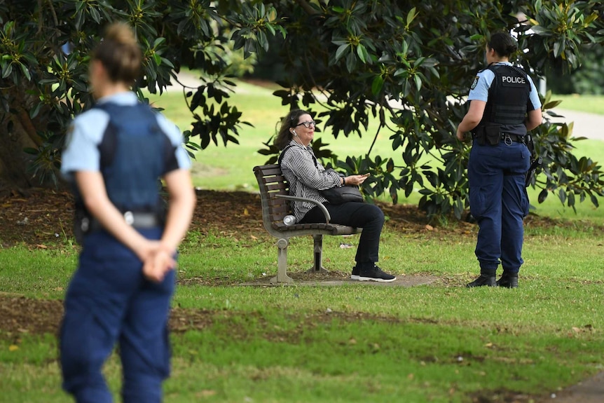 A police officer speaks to a woman sitting on an outdoor bench during the coronavirus outbreak