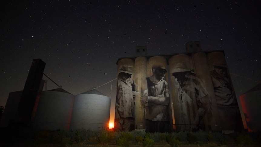 The grain silos at Brim at night time with the moon rising on the horizon, peaking through the silos
