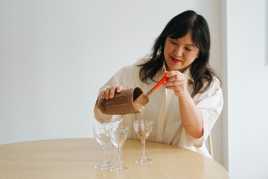 Hetty Lui McKinnon pours chocolate mousse into four stemmed glasses from a blender. A vegan dessert.