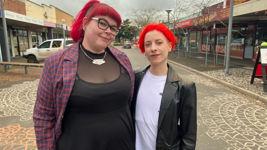 Two young women standing in a street with shops in the background