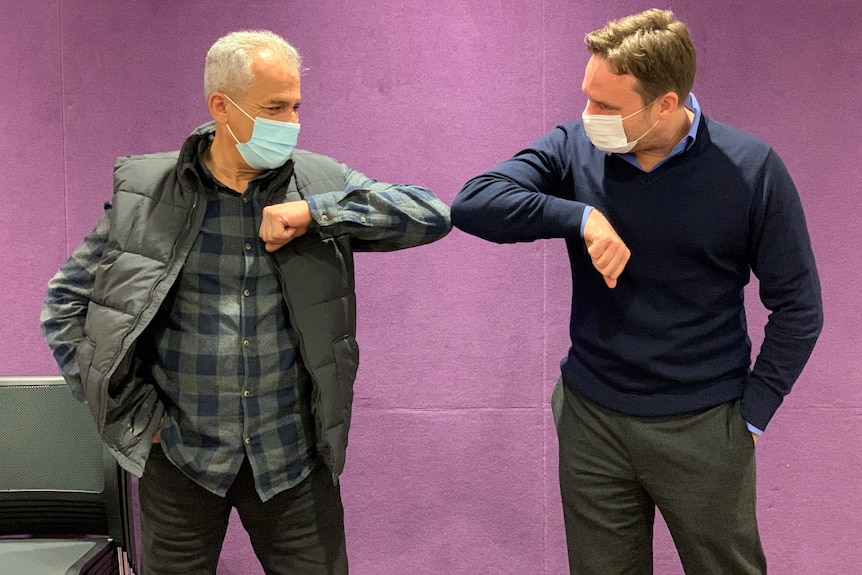 two men, one older and the other younger, wearing masks and hitting their elbows together