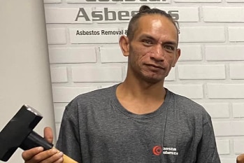 A man in a grey t-shirt holding a hammer 