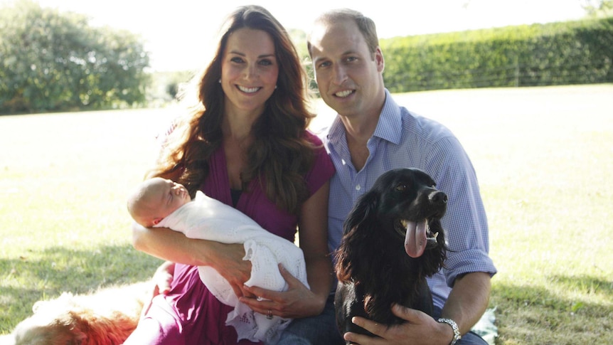 Kate Middleton and Prince William pose holding their baby George with a black dog.