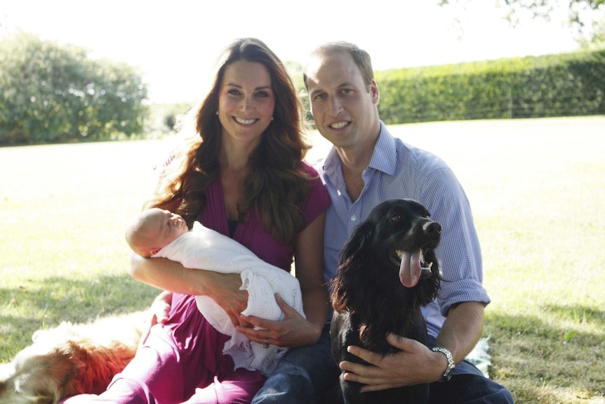 Kate Middleton and Prince William pose holding their baby George with a black dog.