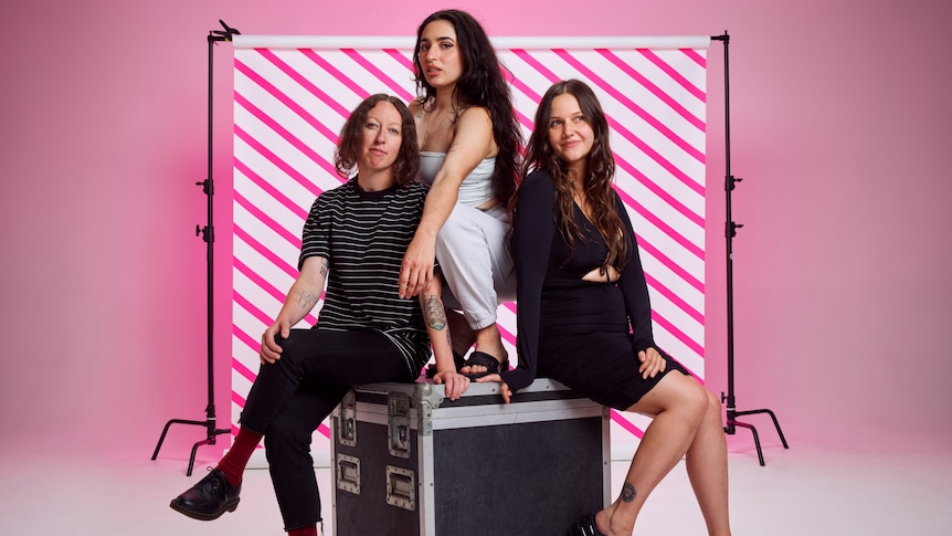 Camp Cope sitting at photoshoot with pink backdrop