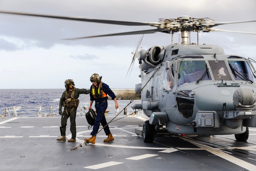 Two people walk from a helicopter on a ship landing deck