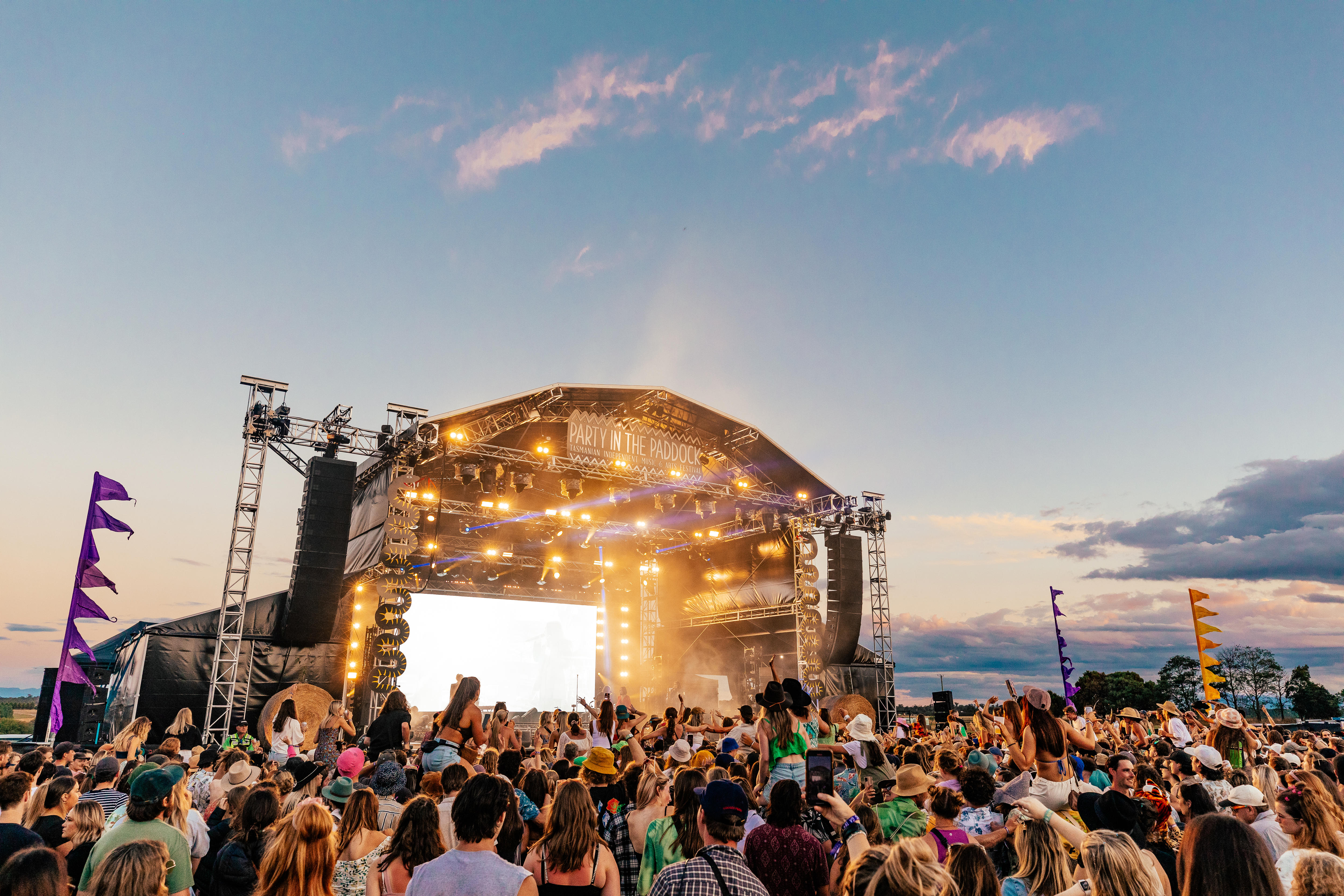 A crowd stands in front of an open air stage at a music festival
