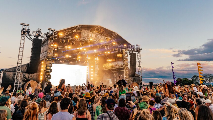 A crowd stands in front of an open air stage at a music festival