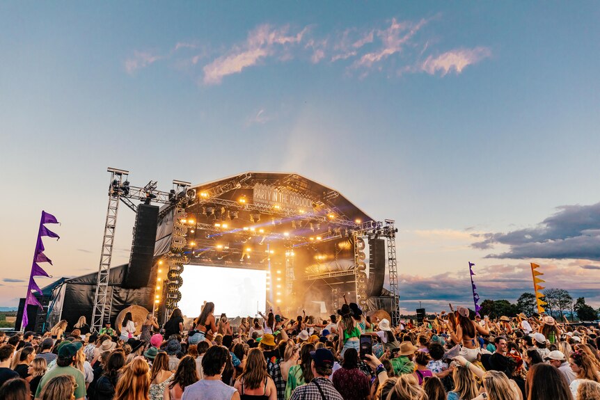 A crowd stands in front of an open air stage at a music festival.