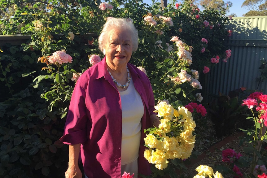 Margot White from Broken Hill stands in front of her rose bushes holding a bunch of yellow blooms.