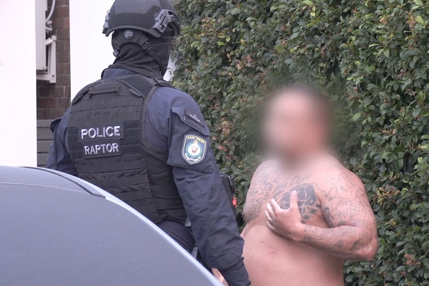 A man's face is blurred who speaks with a police officer who has military gear on 