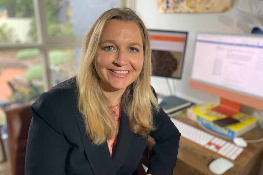 A woman with long, blonde hair, smiling, at her home office in Melbourne.