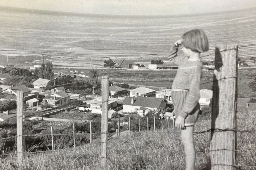 A black and white photo of a young girl looking at the ocean