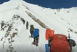 Seven climbers are seen with the eighth holding the camera. The sky ahead is blue and the mountain is covered with snow.