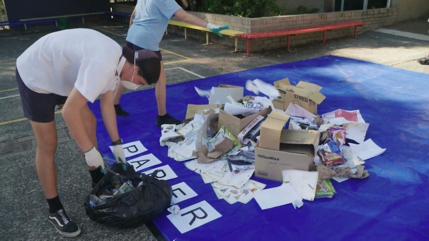 Students pile paper and cardboard waste into a pile on a large tarpaulin
