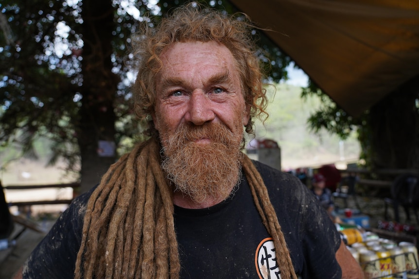 Man with curly red hair, beard and dreadlocks and bright blue eyes looks into the camera.