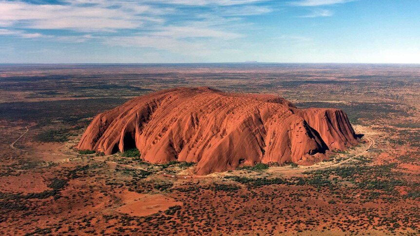 A large, red rock formation surrounded by red, flat, arid land.