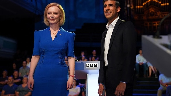 Liz Truss is dressed in a blue dress while Rishi Sunak is dressed in a suit at televised debate. 