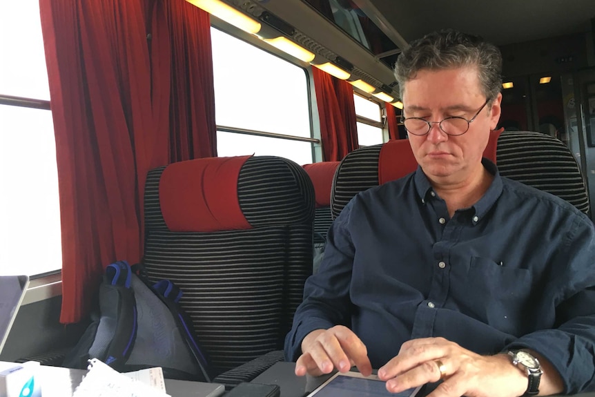 A man in a black shirt reading on a train.