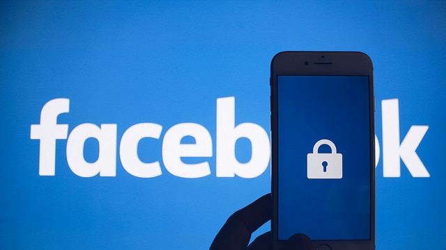 The Facebook logo covered by a silhouetted hand, holding a mobile phone.