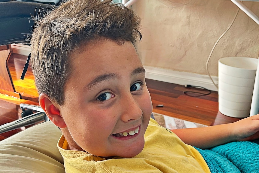 Boy in t-shirt looks over his right shoulder at camera smiling cheekily