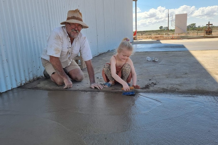 A young girl and an older man apply the finishing touches to a slab of wet cement. 