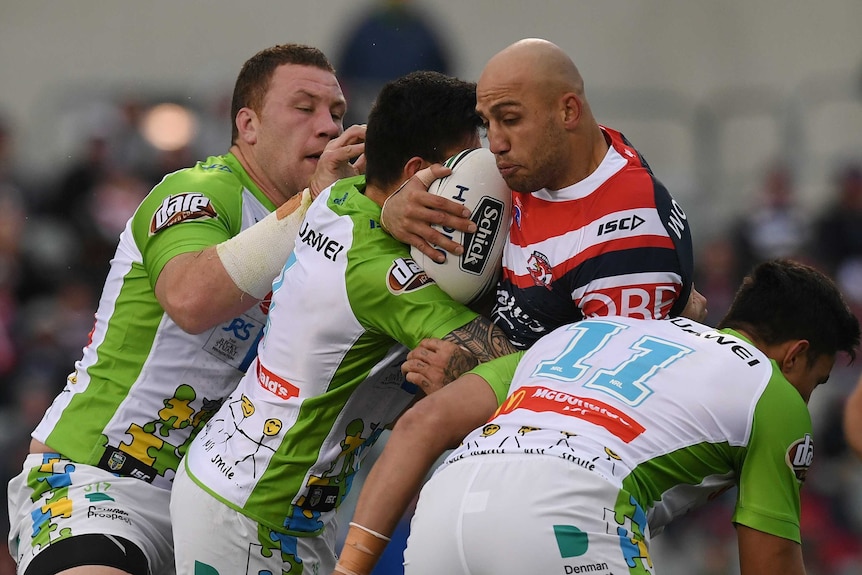Blake Ferguson is held up in a tackle by three Raiders players.