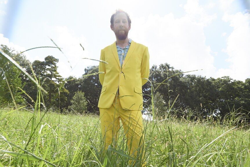 Musician Ben Lee, wearing a yellow suit, stands in long grass.