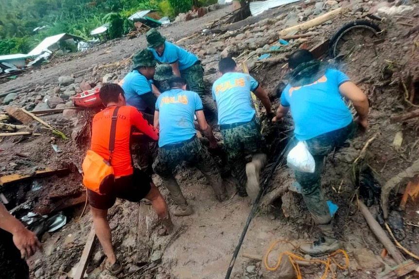 Six men search through a mudslide filled with debris, looking for bodies.