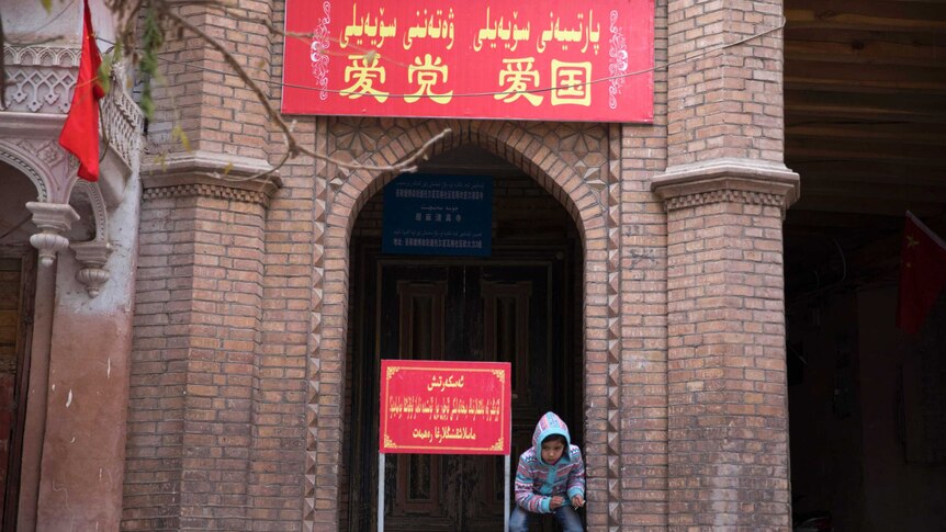 A child rests near the entrance to a mosque where a banner in red reads "Love the party, Love the country".