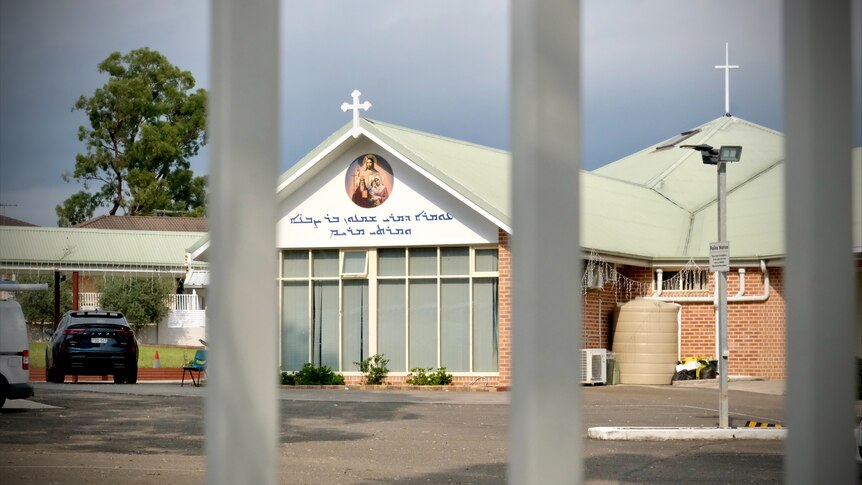 The front of the building at Christ of the Good Shepperd Church through bars of a gate.