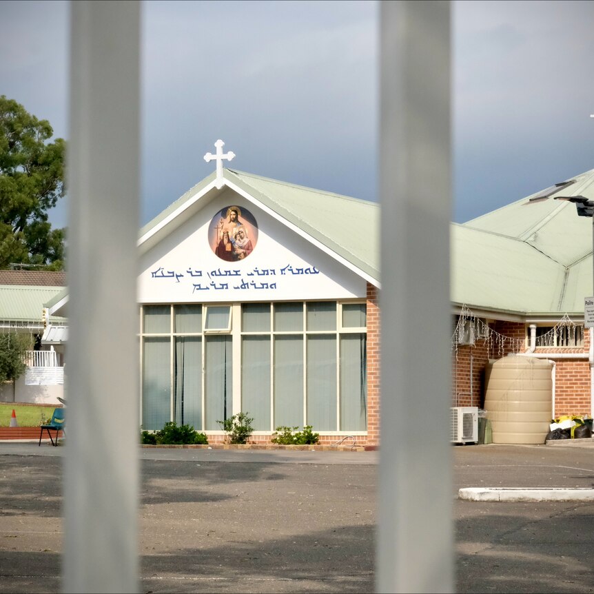 The front of the building at Christ of the Good Shepperd Church through bars of a gate.