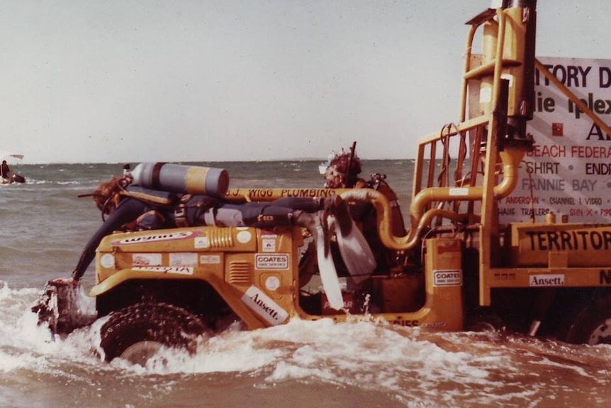 A heavily modified vehicle is driven in shallow water with three people dressed in diving gear on board.