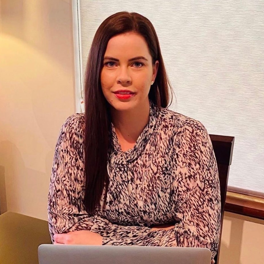 Ricci smiles while sitting at a table with a laptop in front of her.