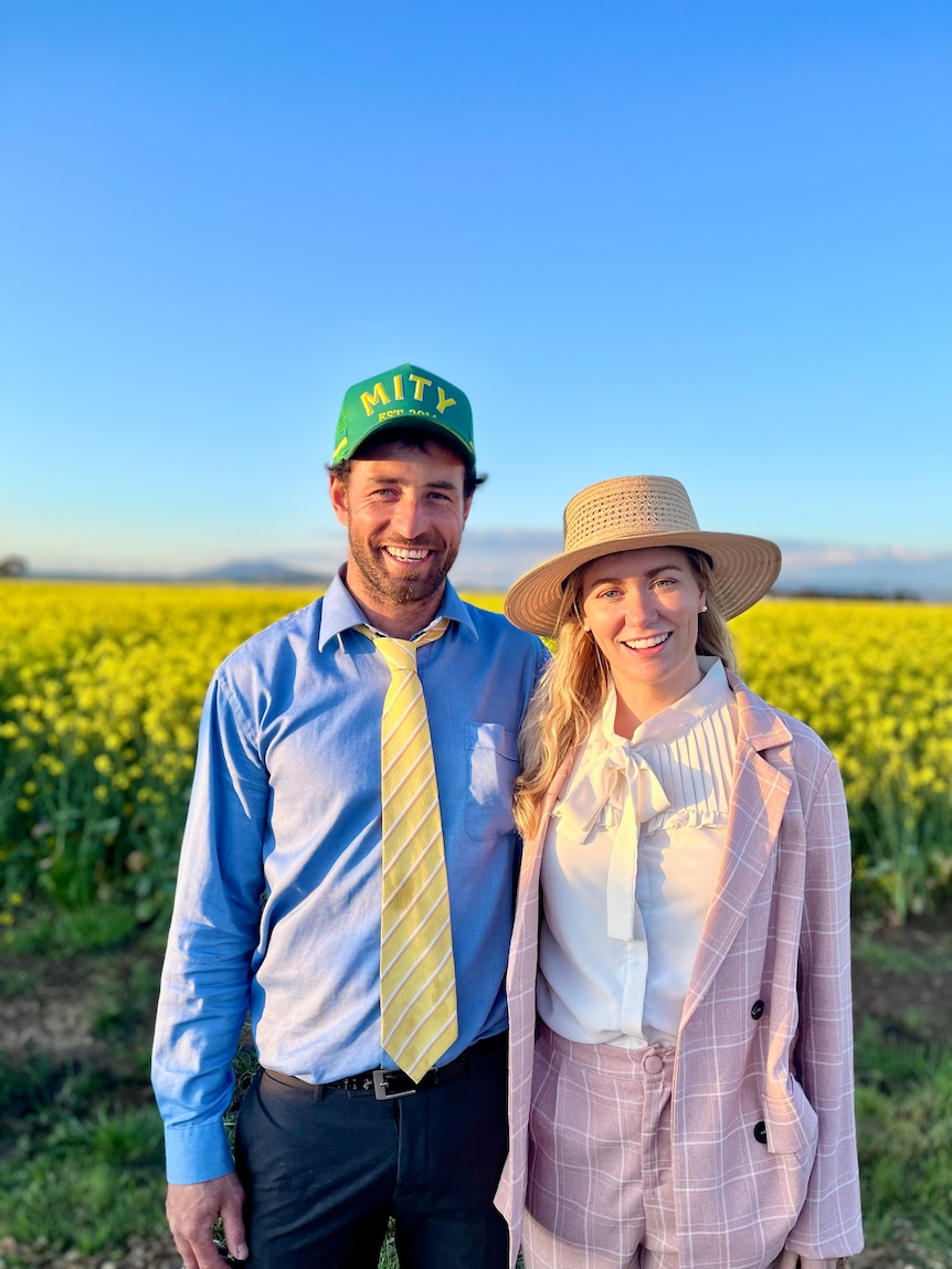 A man and woman in cocktail attire stand in front of a crop of canola, both smiling