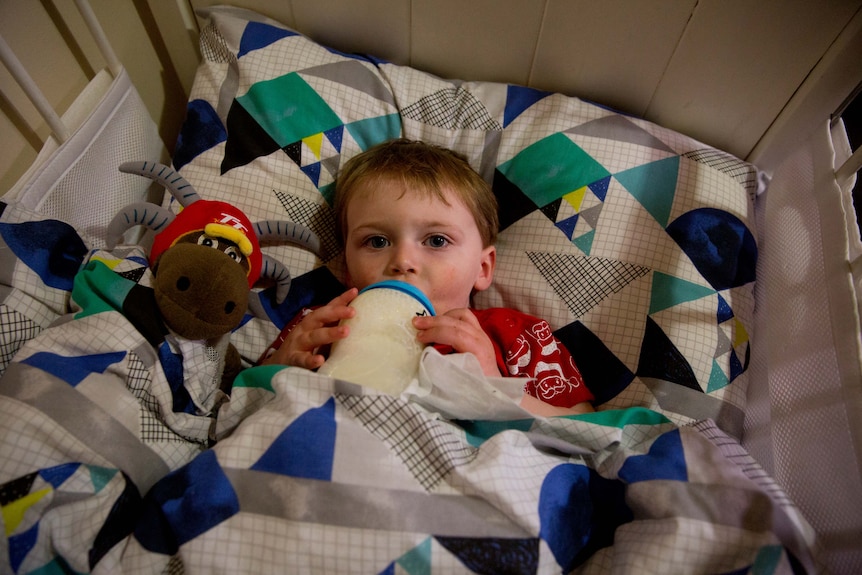 Roman drinks a bottle in his cot.