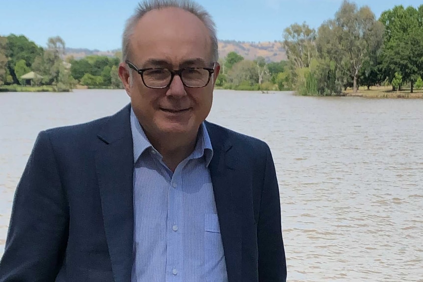 Casually dressed man in jacket, stands with his hands in his jeans pocked by a dam