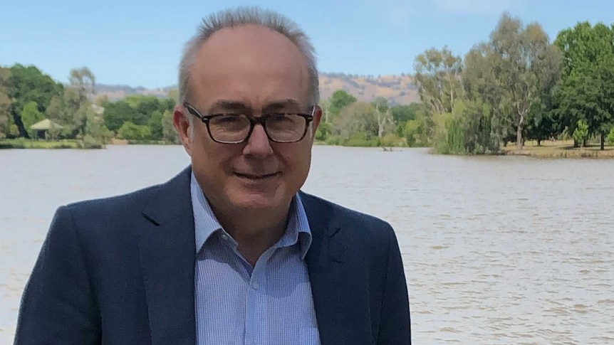 Casually dressed man in jacket, stands with his hands in his jeans pocked by a dam