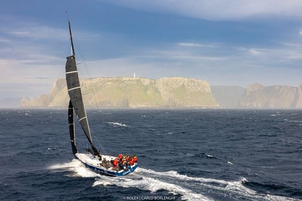 A yacht racing past an island.